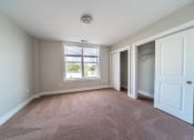 Thumbnail 19 of 22 - Bedroom with large window, beige plush carpeting, double closets, and tan walls.