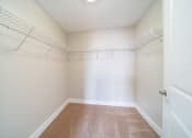 Thumbnail 15 of 22 - Walk in closet with white wire shelving, plush carpeting, and cream walls.