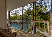 Thumbnail 12 of 26 - A balcony with a chair and a view of a pool and trees.