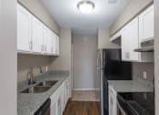 Thumbnail 1 of 16 - Galley-style  kitchen with granite speckled grey/white counters, white cabinets with pull handles on both lower and upper, hardwood-like flooring and stainless appliances
