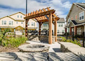 Thumbnail 15 of 37 - A wooden pergola is in the middle of a courtyard with a fire pit.