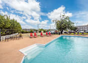 Thumbnail 11 of 47 - A large outdoor swimming pool surrounded by red chairs and trees.