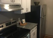 Thumbnail 7 of 14 - Kitchen with white cabinets, grey counter tops, hardwood like flooring, grey walls, and stainless steal stove and fridge.
