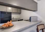 Thumbnail 6 of 10 - A kitchen with a black refrigerator, a counter with a plate of food on it, and a chair.