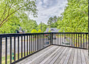 Thumbnail 9 of 25 - A wooden deck with a black railing and trees in the background.