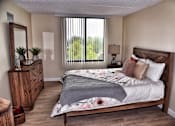 Thumbnail 11 of 14 - A bedroom with a large bed, wooden dresser, and a window with blinds.