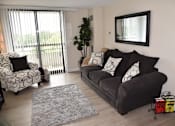 Thumbnail 14 of 14 - A living room with a grey couch and a grey and white patterned chair.