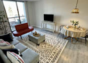 Thumbnail 2 of 14 - A living room with a red chair, a white table, and a television.