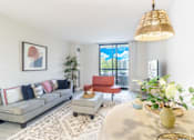 Thumbnail 6 of 14 - A living room with a grey couch, a red chair, a coffee table, and a large window with a view of the trees outside.