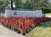 Thumbnail 5 of 12 - a sign for the village club apartments in front of a flower garden at Village Club on Franklin, Southfield, MI