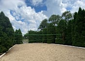 Thumbnail 11 of 12 - a volleyball court in a park with trees and a cloudy sky at Village Club on Franklin, Southfield Michigan