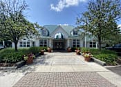 Thumbnail 4 of 12 - the front of a white building with a walkway and potted plants at Village Club on Franklin, Southfield, MI 48034