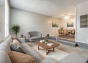 Thumbnail 5 of 50 - A living room with a grey couch, a grey armchair, a wooden coffee table, and a dining table with chairs.