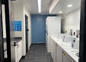 Thumbnail 14 of 23 - A public restroom with a blue wall and white sinks.