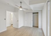 Thumbnail 9 of 33 - A room with a ceiling fan and light, wooden floors, and white walls with doors on either side.