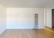 Thumbnail 9 of 12 - A room with a wooden floor and a white wall with a door on the right side.
