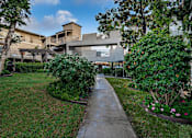 Thumbnail 32 of 46 - A concrete pathway leads to a building surrounded by greenery.