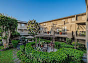 Thumbnail 1 of 46 - A courtyard with a tree, a bench, and a table surrounded by buildings.