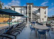 Thumbnail 2 of 11 - A patio with tables and chairs and a building in the background.