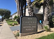 Thumbnail 1 of 4 - A sign for Chateau Woodland Manor is displayed in front of a building.