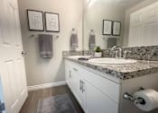 Thumbnail 22 of 35 - A bathroom with a marble countertop and white cabinets.
