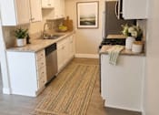 Thumbnail 11 of 20 - A kitchen with white cabinets and a rug on the floor.