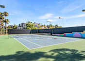 Thumbnail 10 of 67 - A tennis court with a blue surface and white lines, surrounded by a wall with colorful circles and a fence.