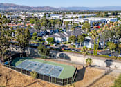 Thumbnail 7 of 67 - A tennis court is surrounded by houses and grass trees.