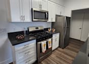 Thumbnail 17 of 23 - A kitchen with white cabinets and a black countertop.