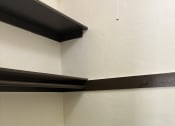 Thumbnail 24 of 35 - the corner of a room with white walls and a black shelf
