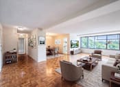Thumbnail 4 of 15 - A spacious living room with a large window and a view of trees outside.
