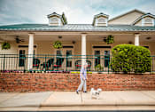 Thumbnail 75 of 109 - A woman walking her dog in front of a house with a green roof.