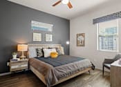 Thumbnail 10 of 36 - A bedroom with a bed, nightstand, chair, and pictures on the wall.