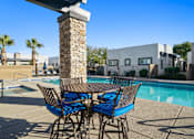 Thumbnail 28 of 36 - A table with chairs is in the foreground of a pool area.