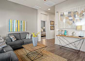 Thumbnail 6 of 36 - A living room with a grey couch, a coffee table, and a painting on the wall.
