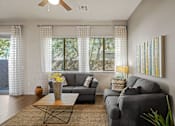 Thumbnail 8 of 36 - A living room with a grey couch, a coffee table, and a painting on the wall.