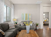 Thumbnail 9 of 36 - A living room with a grey couch, a wooden coffee table, and a painting on the wall.