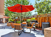 Thumbnail 10 of 40 - A red umbrella is in the middle of a patio with chairs and a table.