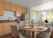 Thumbnail 7 of 44 - Downtown San Jose, CA Apartments - Vendome Place - Open Floor Plan Kitchen with Luxury Vinyl Tile Flooring, Stainless Steel Appliances, Brown Flat-Panel Cabinets, Round Dining Table with Chairs, and View of Living Area.