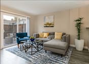 Thumbnail 13 of 27 - A living room with a grey couch, a blue chair, a coffee table, and a painting on the wall at Nola 624 Apartments, West Covina, California