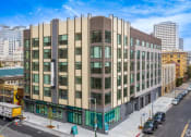Thumbnail 29 of 30 - 1 Bedroom Luxury Apartments in Downtown Oakland CA - Alice House - Property Exterior During the Daytime, with Grey and Tan Walls, Windows, and Street View