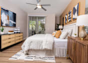 Thumbnail 43 of 98 - Spring Valley, NV, 89147 Apartments for Rent - Alicante - Inviting Bedroom With Cozy Bed, Ceiling Fan, Wood Dresser, And Sliding Glass Door With Vertical Blinds Leading To Private Patio.