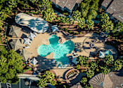 Thumbnail 6 of 98 - Three-BR Apartments in Spring Valley, NV - Alicante - Aerial View Of Resort Style Pool With Curved Design, Lounge Seating, Shaded Cabanas, And Palm Lined Courtyard Surrounded By Buildings