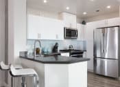 Thumbnail 17 of 29 - Kitchen with stainless steel appliances and bar seating at Aqua Via Apartments, Oakland, CA