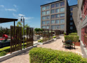 Thumbnail 12 of 29 - a courtyard with tables and chairs and a building in the background at Aqua Via Apartments, Oakland