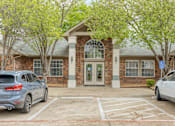 Thumbnail 2 of 29 - A parking lot in front of a brick building with two cars parked.