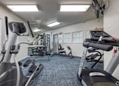 Thumbnail 17 of 29 - A gym with a variety of equipment including treadmills, elliptical machines, and a television.
