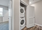 Thumbnail 34 of 83 - A white washing machine and dryer are stacked in a small laundry room.