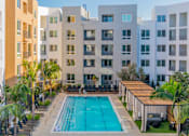 Thumbnail 2 of 29 - A swimming pool surrounded by lounge chairs and palm trees in front of apartment buildings. at Baker Block, Costa Mesa, CA
