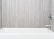 Thumbnail 6 of 26 - A white bathtub in a bathroom with grey tiled walls at Wilshire Valencia Apartment, Los Angeles, CA